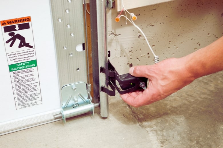 Someone checking the safety sensors of a garage door is part of garage safety.