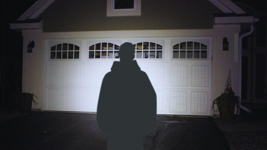 A man shining a flashlight on a garage door during a power outage. Know how to lock a garage door during a power outage.